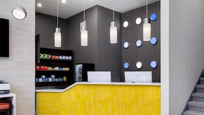 Un comptoir d’accueil avec deux ordinateurs portables, un plan de travail jaune à motifs et des luminaires suspendus au plafond.