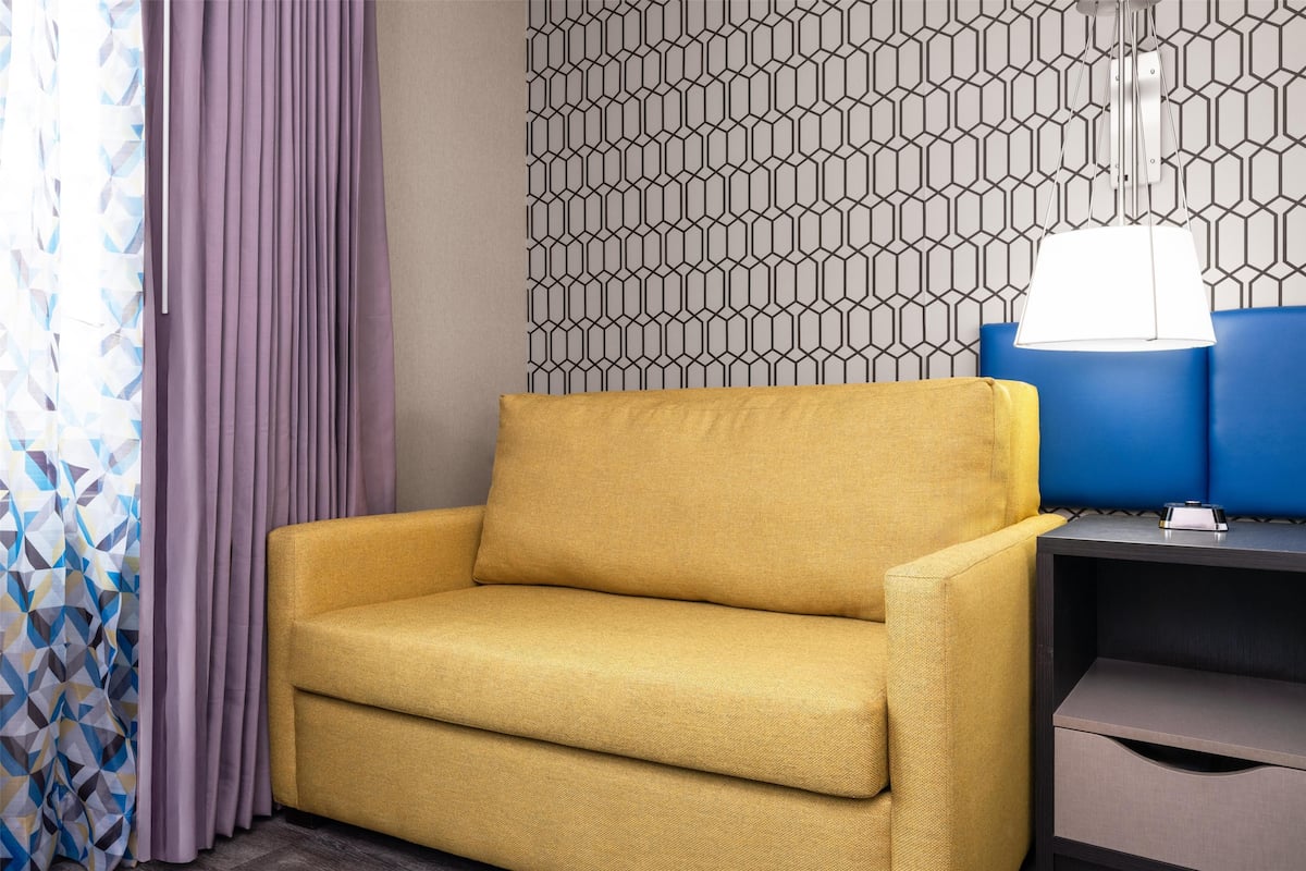 Un canapé jaune, une chaise bleue, un mur à motifs et une lampe suspendue.
