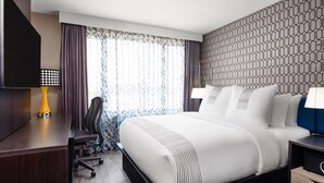 Une chambre d’hôtel avec un grand lit, un bureau avec une chaise, une télévision et un mur décoré d’un motif.
