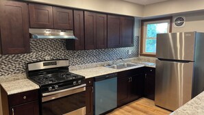 A modern kitchen with dark wood cabinets, a stainless steel stove, and a built-in dishwasher. - Charming remodeled 2-bedroom furnished home in safe, delightful Menomonee Falls (Menomonee Falls)