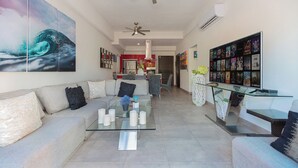 Ein modernes Wohnzimmer mit einem Glastisch, einer Couch, einem Deckenventilator und einem Wand-Fernseher, der Filmplakate zeigt.