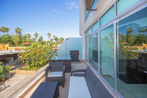 Un patio moderno al aire libre con mobiliario de mimbre, paredes de vidrio y vista a palmeras.