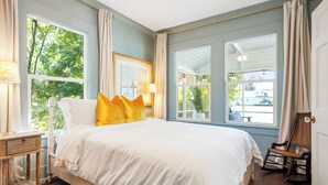 A bedroom with a large bed, two windows, a chair, and a nightstand. - Beautifully restored cottage downtown Historic Brunswick close to golf + beaches (Brunswick)