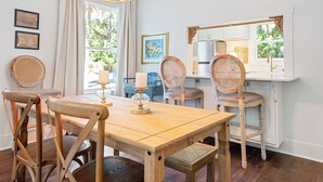 A dining area with a wooden table and chairs, a chandelier, and a window with a view of greenery. - Beautifully restored cottage downtown Historic Brunswick close to golf + beaches (Brunswick)