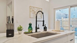 A modern kitchen with a large sink, a set of knives, a potted plant, and a decorative wall piece.