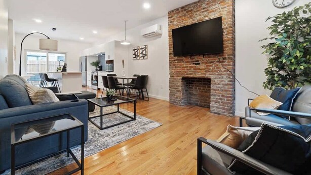 A modern living room with a brick fireplace, a flat-screen TV mounted on the wall, and a dining area with a table and chairs.