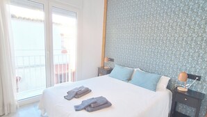 A bedroom with a large bed, a nightstand, a lamp, and a view of the outside through a sliding door. - THE PORT. E151A VacaHome Management (El Puerto de Santa María)