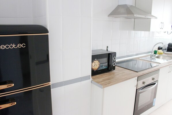 Une cuisine moderne avec des meubles blancs, un réfrigérateur noir, un four à micro-ondes et un four en acier inoxydable.
