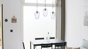 Un salon moderne avec un coin repas, comprenant un canapé, une table à manger, des chaises, des luminaires suspendus et une fenêtre avec des rideaux.