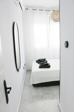 Une chambre à coucher moderne et minimaliste, avec un grand lit, un miroir et un luminaire en osier.