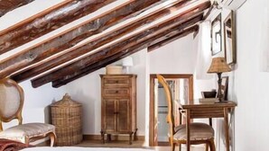 Une chambre avec un plafond en pente, des poutres en bois, un lit, une chaise, une petite table et un meuble.