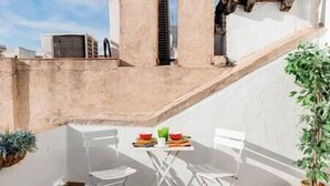 Un petit espace extérieur aménagé pour prendre les repas, avec une table et deux chaises, un pot de fleurs et un escalier.