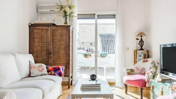 Un salon avec un canapé blanc, une table basse, un téléviseur et une fenêtre donnant sur l’extérieur.