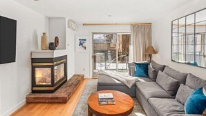 A modern living room with a fireplace, a sofa, a coffee table, and a large window with a view. - Gold-rated 2 Bedroom Condo at the Base of Aspen Mountain (Aspen)
