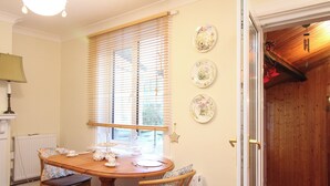 Un coin repas avec une table et des chaises en bois, une fenêtre avec des stores et trois assiettes décoratives accrochées au mur.