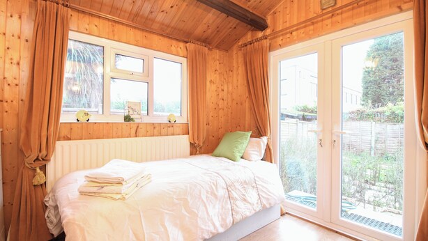 Une pièce en bois avec un lit, deux fenêtres et une vue sur l’extérieur.