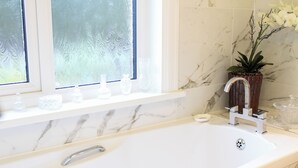 Une salle de bain avec un lavabo en marbre, une fenêtre givrée et une orchidée en pot.