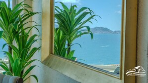 Ein Fenster mit Blick auf das Meer und ein Berg, Zimmerpflanzen und das Logo von Tres Atardeceres.