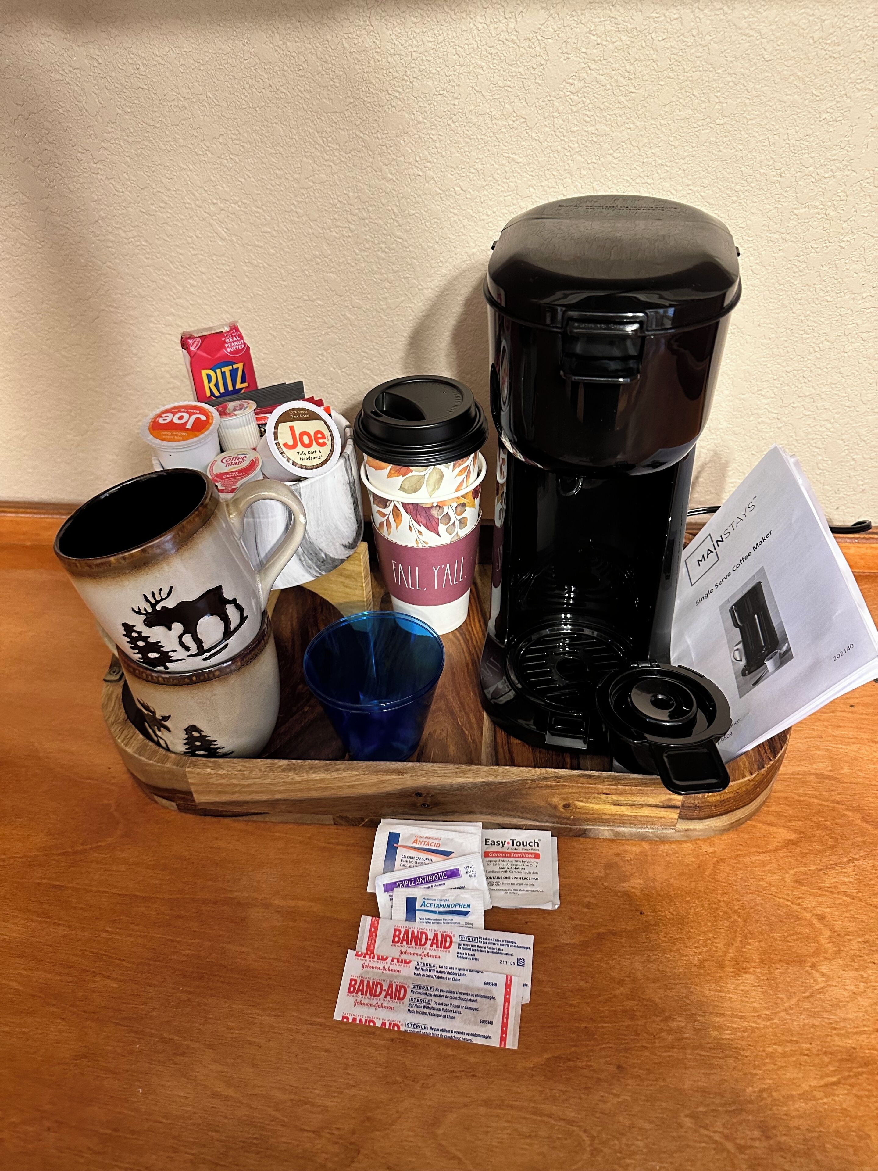 A tray with a coffee maker, a mug with a moose design, a coffee cup with a leaf pattern, a blue cup, and some coffee pods.