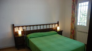 Einzimmer mit einem Einzelbett, einem Holz-Kopfteil, zwei Nachttischlampen, einer grünen Bettdecke und einem Fenster mit Vorhängen.