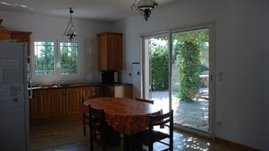 Eine Küche mit Holzausbau, einem Esstisch mit Stühlen, einem Kühlschrank und einer großen Schiebeglastür, die in einen Garten führt.