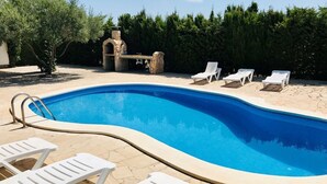 Ein Schwimmbad mit weißen Liegestühlen und einer Steinstruktur im Hintergrund.