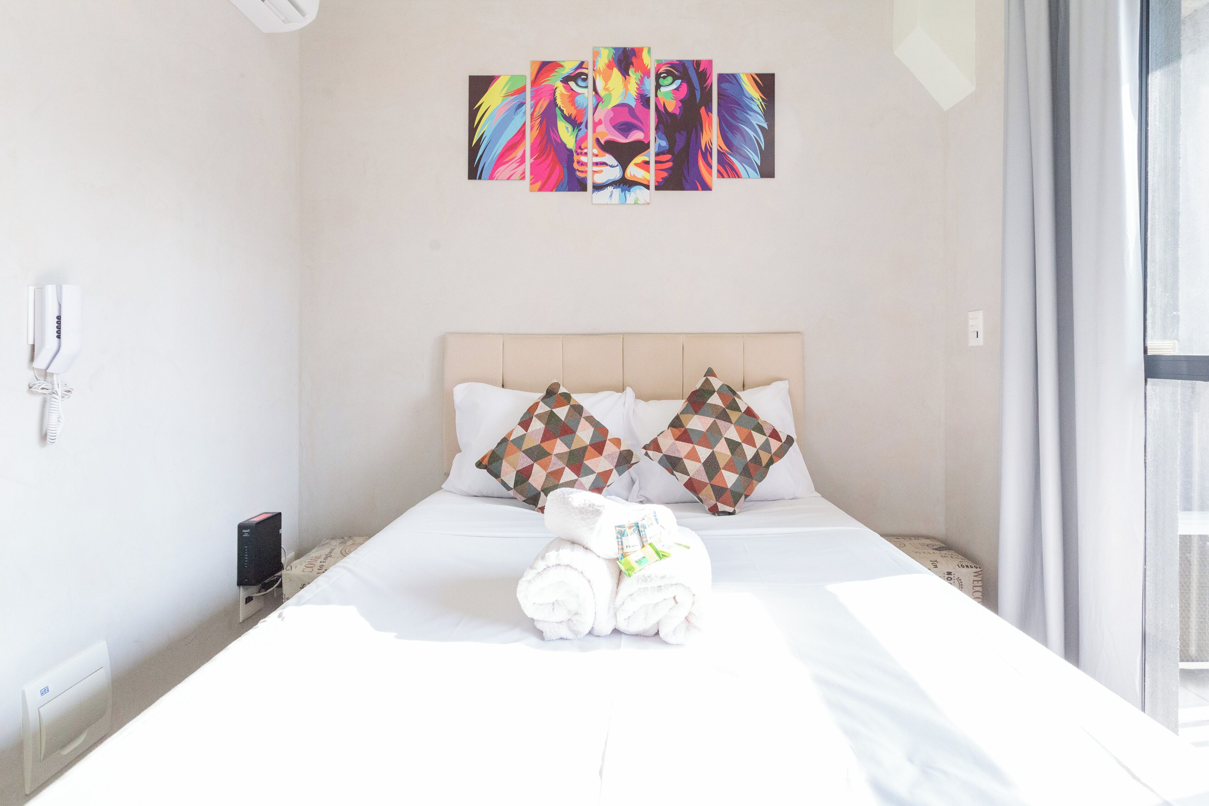 A hotel room with a bed, pillows, a painting, and a window.
