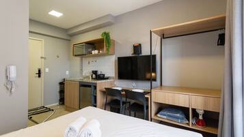 Ett hotellrum med en säng, ett skrivbord, en stol, en TV, en mikrovågsugn, ett handfat och en liten köksdel.
