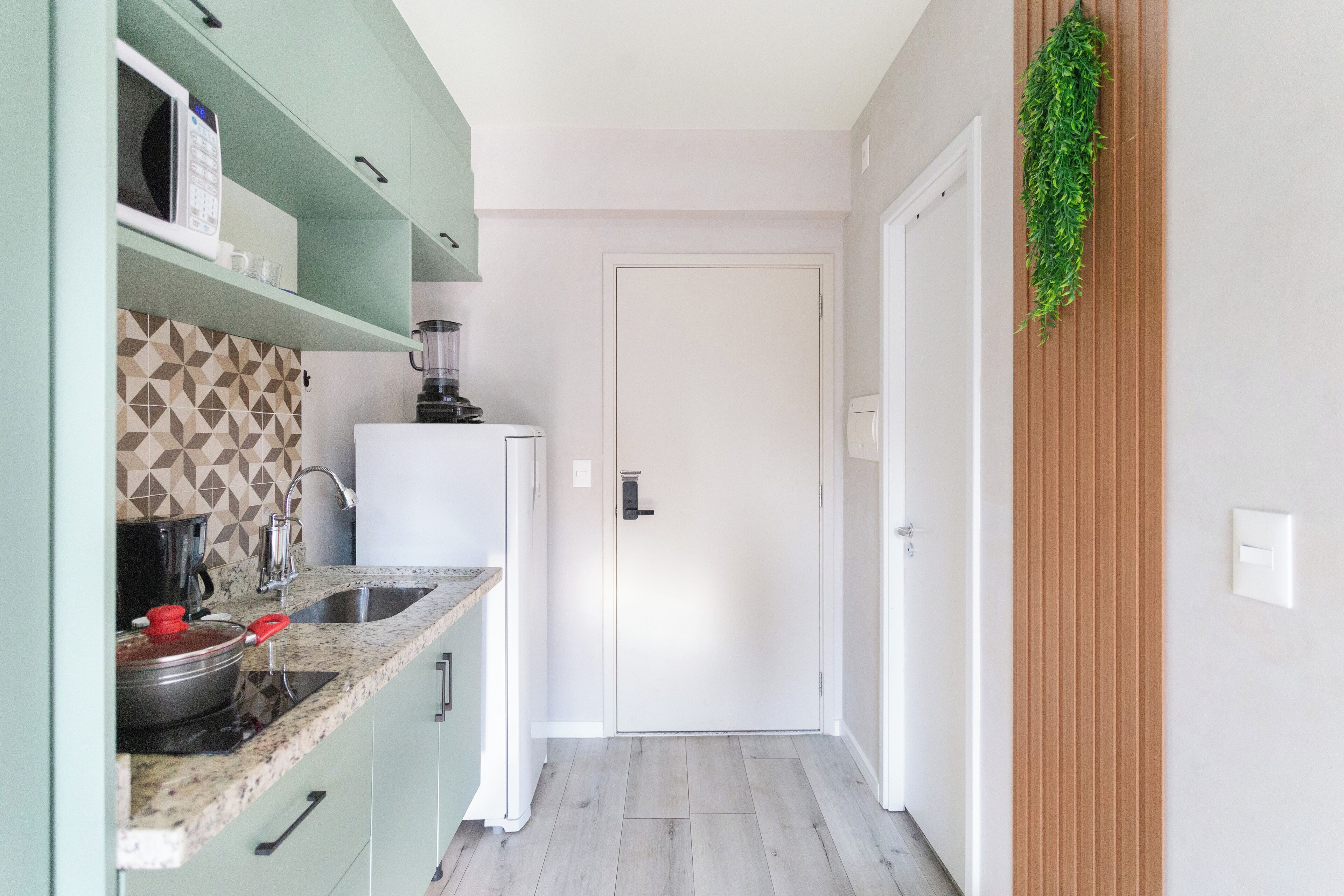 A compact kitchen with a microwave, sink, and stove, a door with a handle, and a wooden panel on the wall.