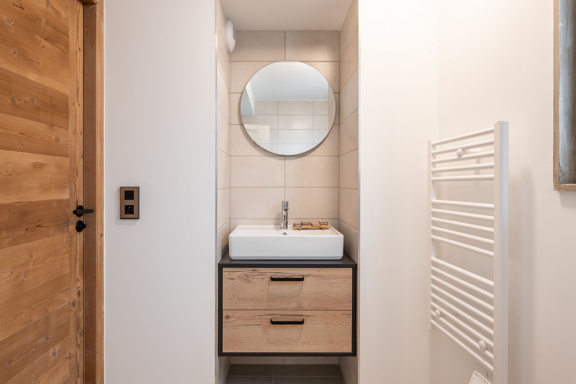 A bathroom with a wooden door, a round mirror, a white sink, and a towel rack.