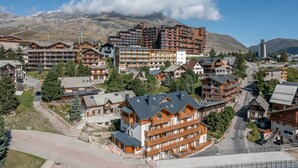A mountain resort with wooden buildings, a central road, and a view of snow-capped mountains.