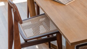 A wooden dining table with a magazine, two wicker chairs, and a view of the outdoors.