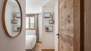 A bedroom with a wooden door, a large mirror, and three wall-mounted shelves with plants.