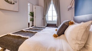 A bedroom with a bed, a large window with curtains, a door, and a wall-mounted picture. - Remparts 2 Bed w Private terrace & sauna (Québec)