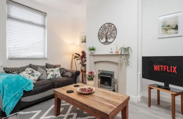 A living room with a sofa, coffee table, fireplace, and a TV displaying the Netflix logo. - Stylish Home Retreat on Outskirts of Liverpool (St Helens)