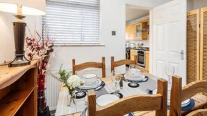 Un coin repas avec une table dressée pour quatre personnes, des chaises en bois, une lampe et une fenêtre avec des stores.