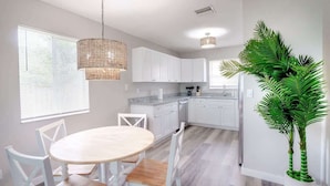 A modern kitchen with white cabinets, a round dining table, and a hanging light fixture.