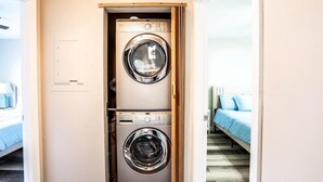 A laundry room with two front-loading washing machines, a bed with blue bedding, and a wooden floor.