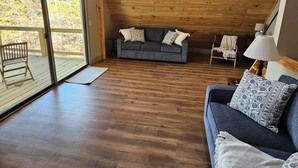 A spacious loft with a wooden ceiling, a gray sofa with patterned cushions, and a view through large sliding glass doors to an outdoor deck. - SMITH LAKE CABIN-Cave, Dock,  (Crane Hill)