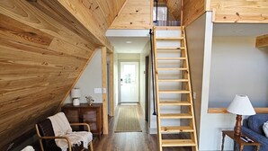 A loft-style room with wooden floors and walls, a loft bed, a wooden ladder, a sofa, a chair, and a lamp. - SMITH LAKE CABIN-Cave, Dock,  (Crane Hill)