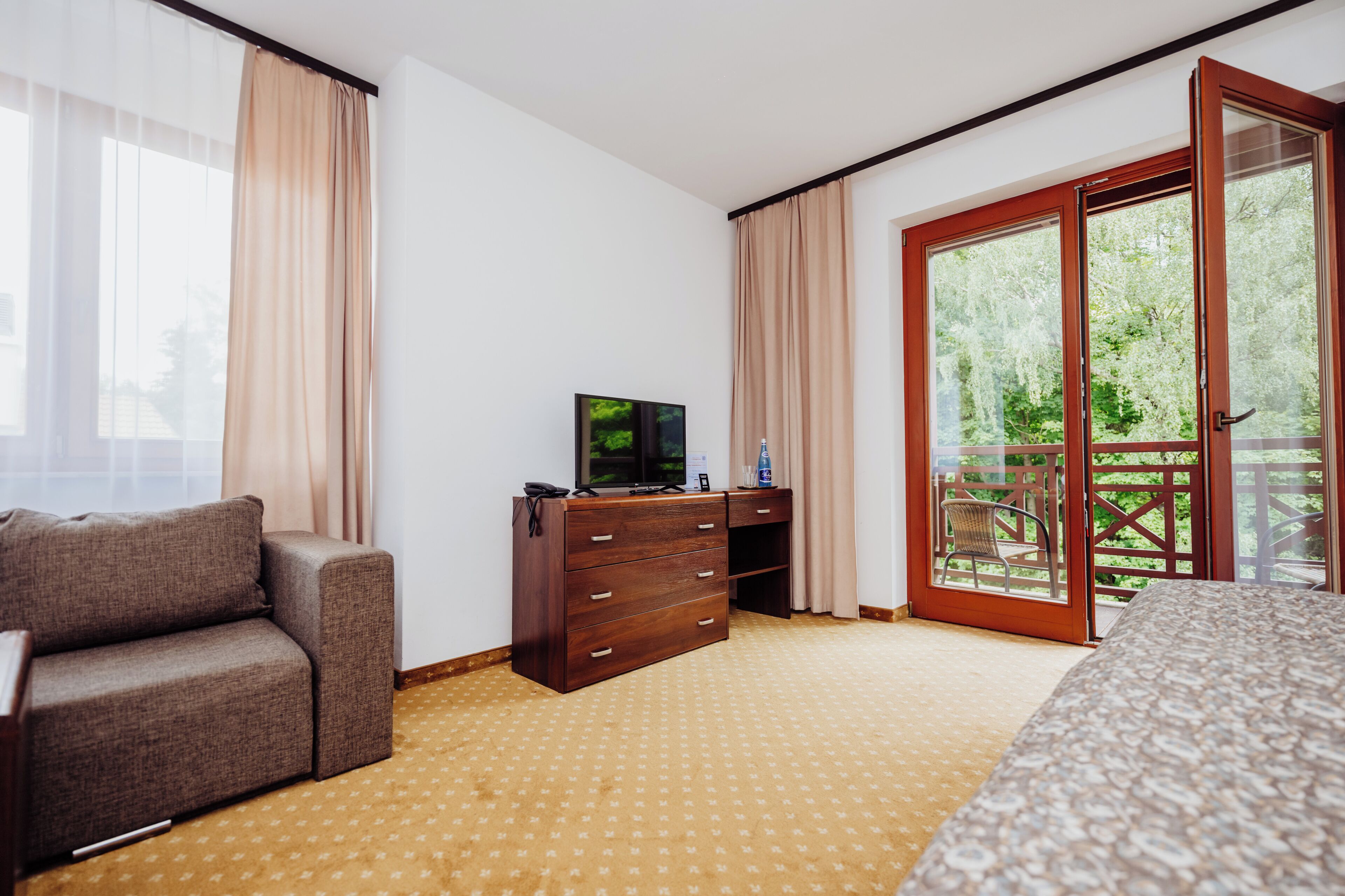 Una habitación de hotel con un sofá, un televisor sobre un aparador de madera, una cama y una puerta corrediza de vidrio que da a un espacio al aire libre.