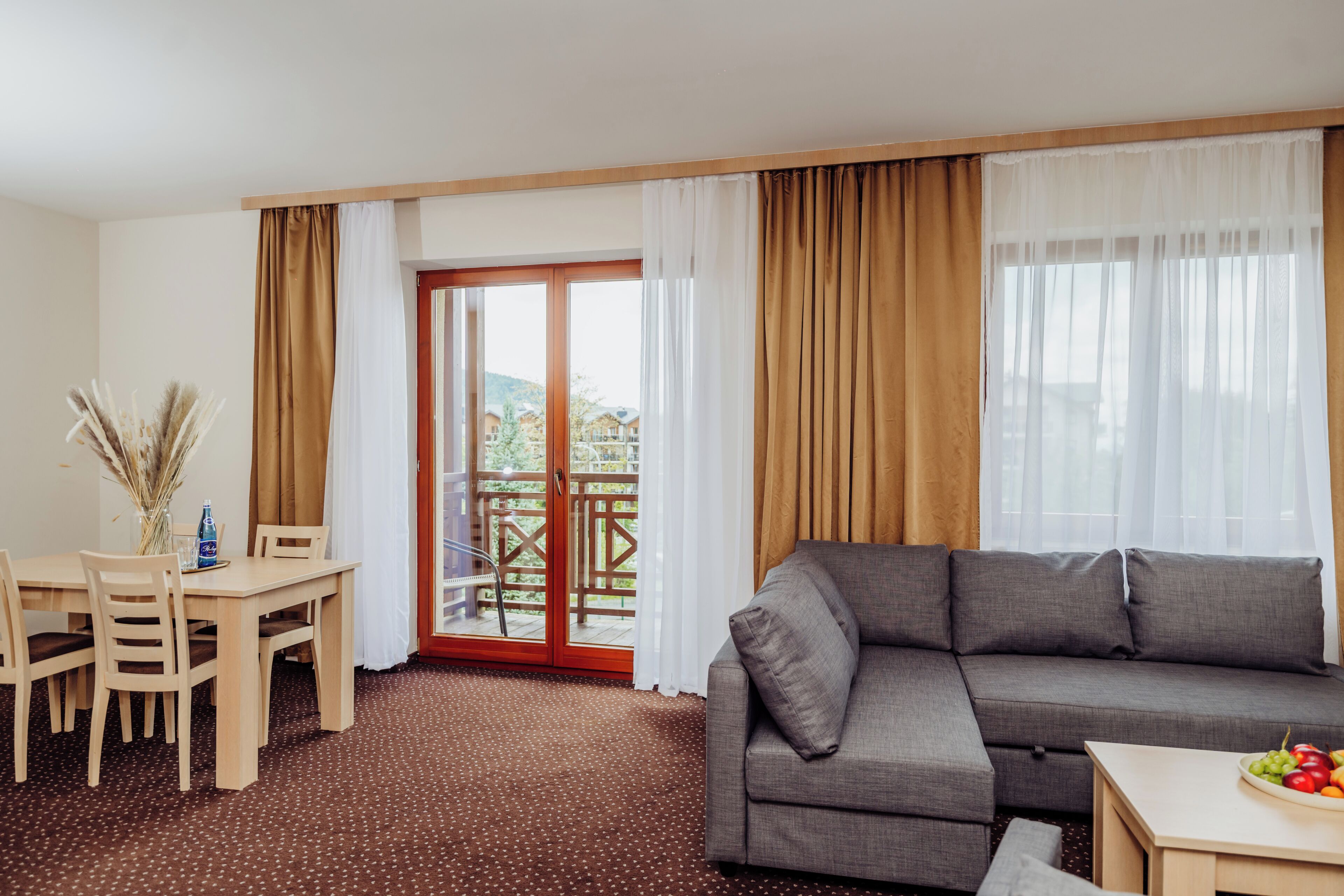 A room with a sofa, a dining table with chairs, a small table with fruit, and a sliding glass door to an outdoor area.
