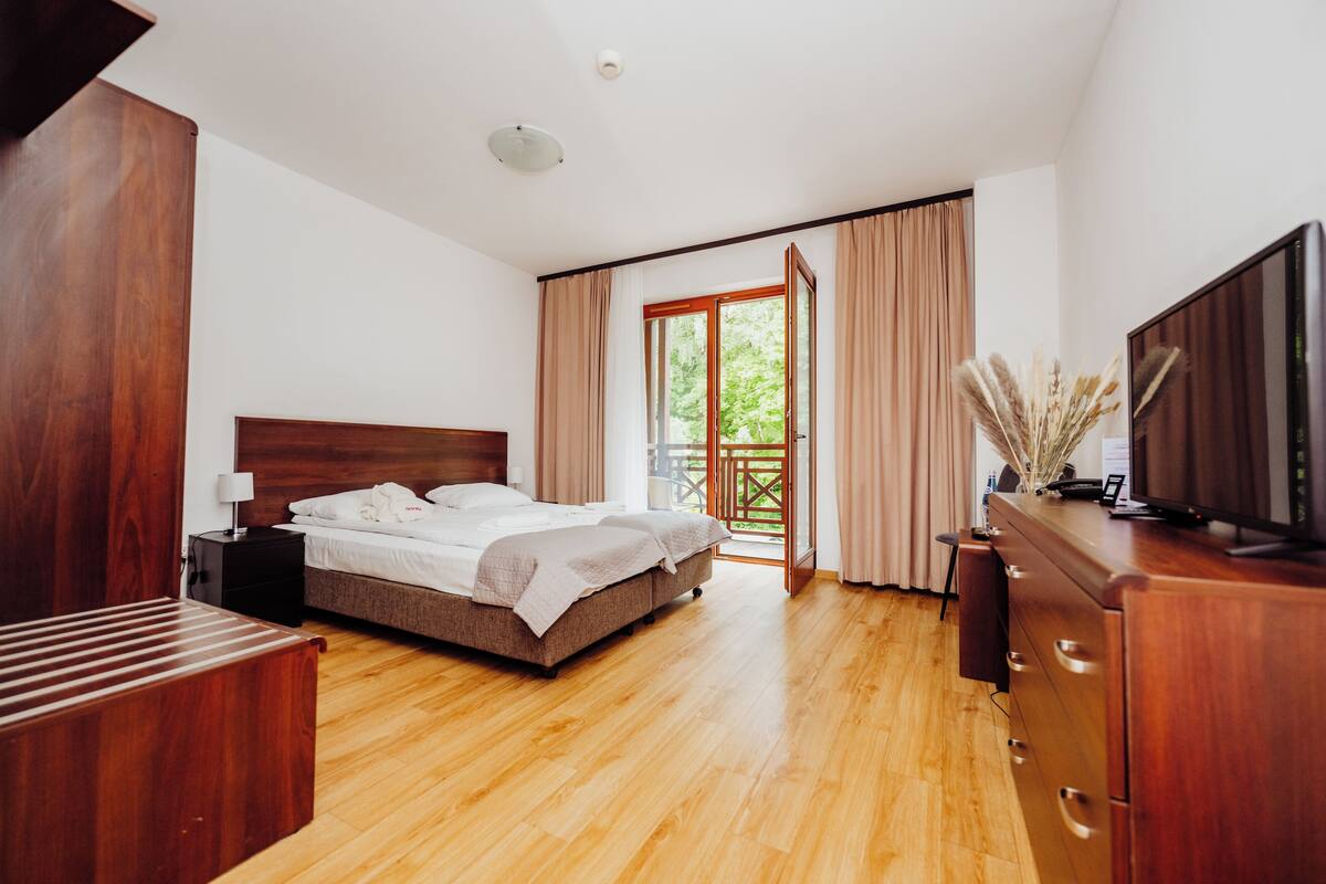 A bedroom with a bed, wooden dresser, TV, and a balcony with curtains.
