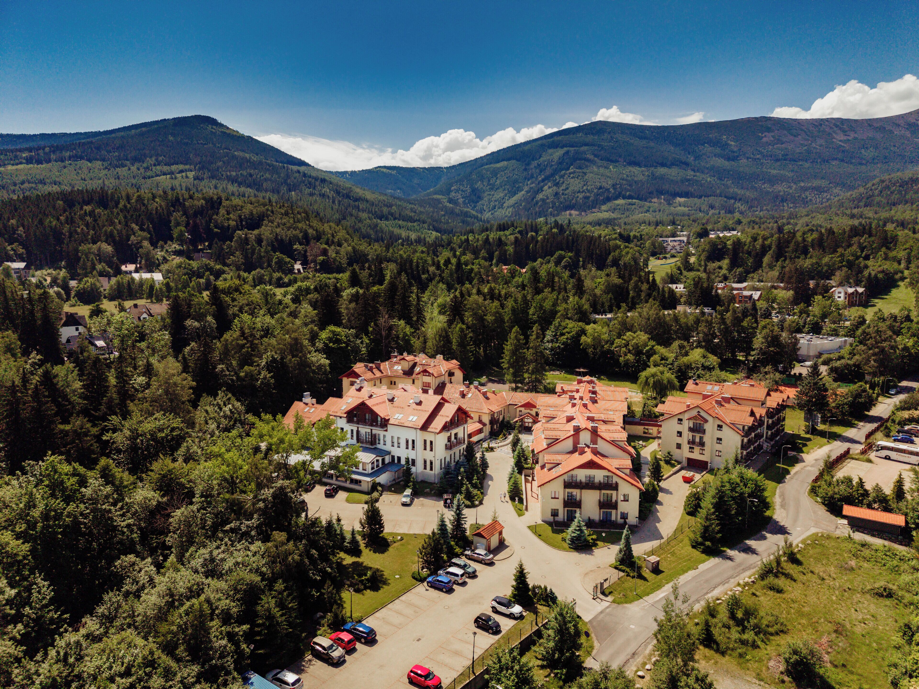 Vista aérea de una zona residencial con varios edificios, carreteras y colinas boscosas circundantes.