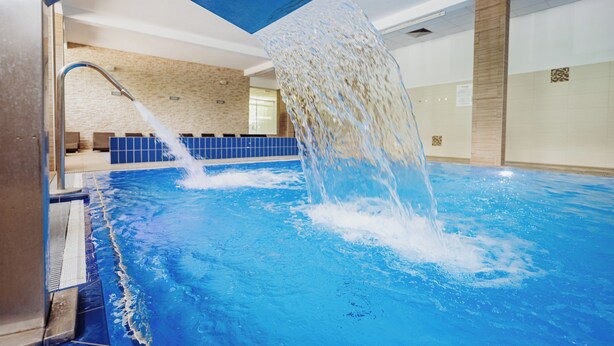 A swimming pool with water flowing from a faucet, a tiled wall, and a wooden column. - Instytut Zdrowia Sofra Fit & SPA Karpacz (Karpacz)