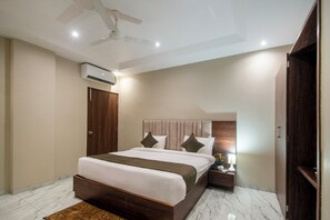 A modern bedroom with a large bed, a ceiling fan, an air conditioning unit, a nightstand with a lamp, and a wooden wardrobe. - Hotel Grand Tulip By Aditya Inn (Jaipur)