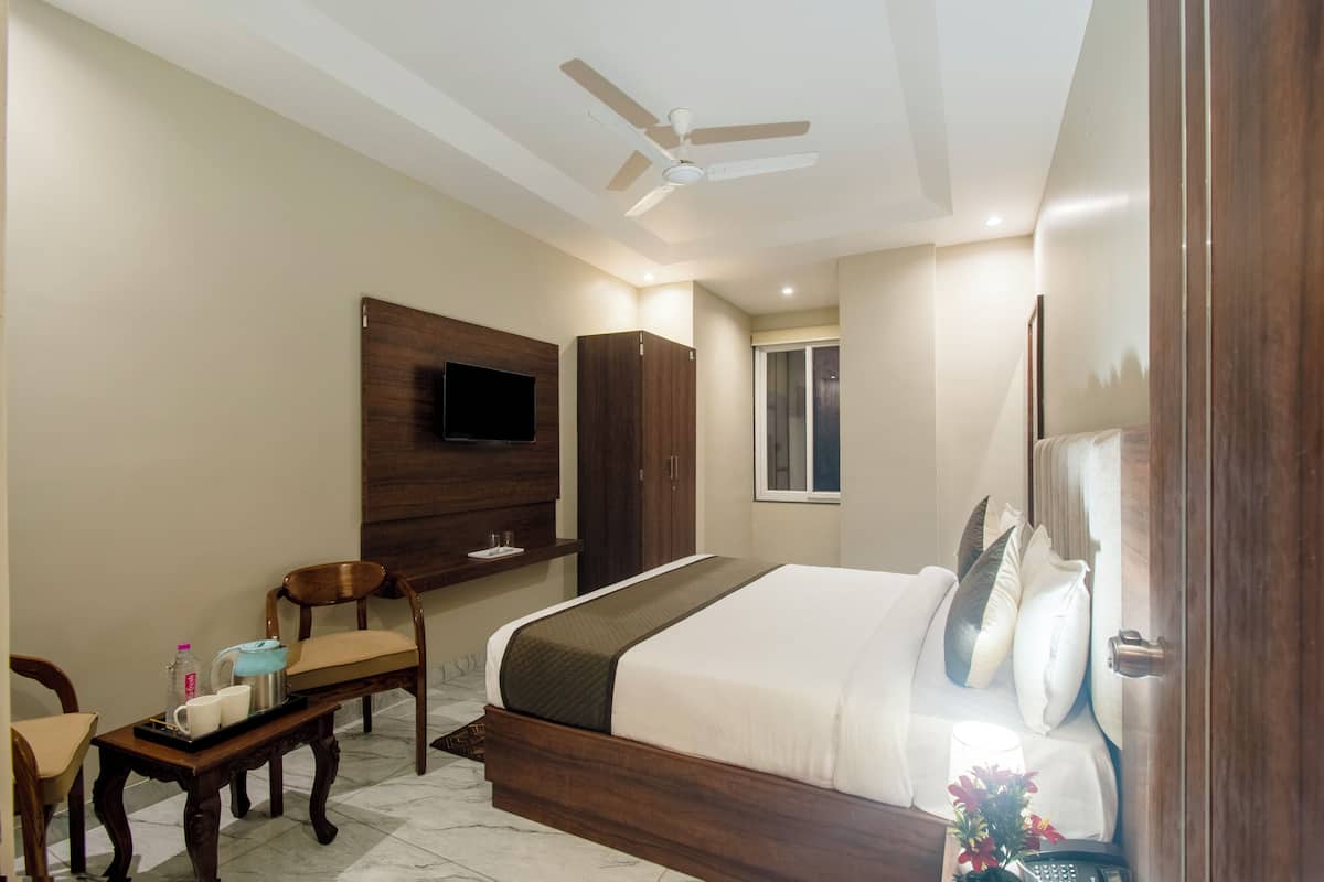 Une chambre à coucher comprenant un lit, un bureau, une chaise, un téléviseur fixé au mur et un ventilateur de plafond.