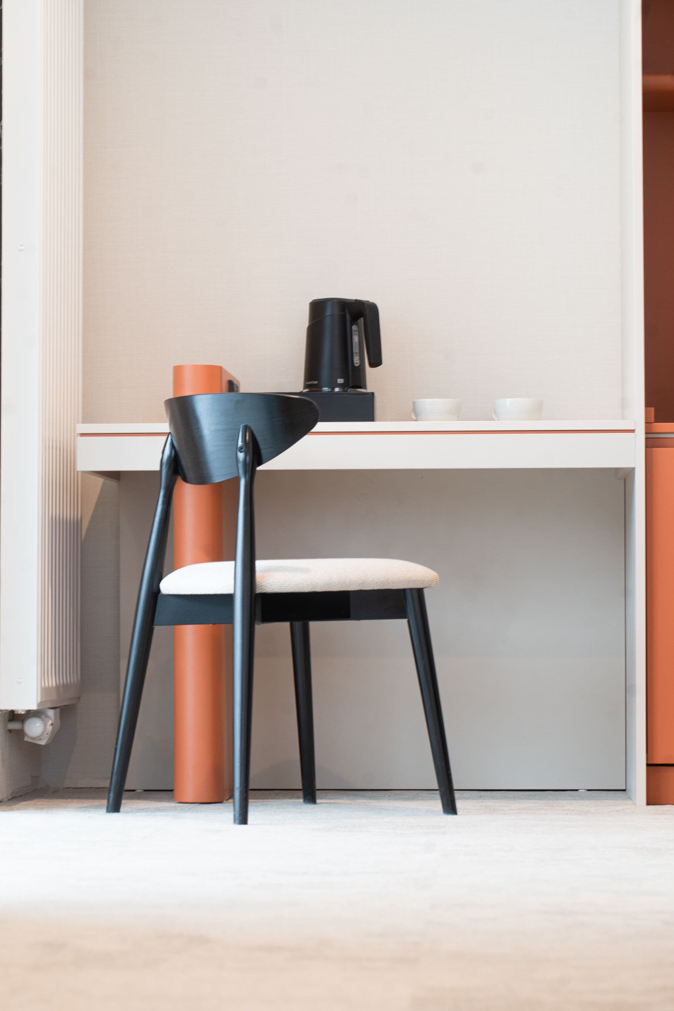 Eine moderne Küche mit weißer Arbeitsplatte, einem schwarzen Stuhl mit orangefarbener Lehne und einer Kaffeemaschine.