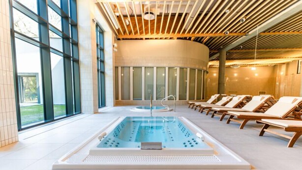 Ein Hallenbad mit Liegestühlen, großen Fenstern und einem modernen Deckenbau.