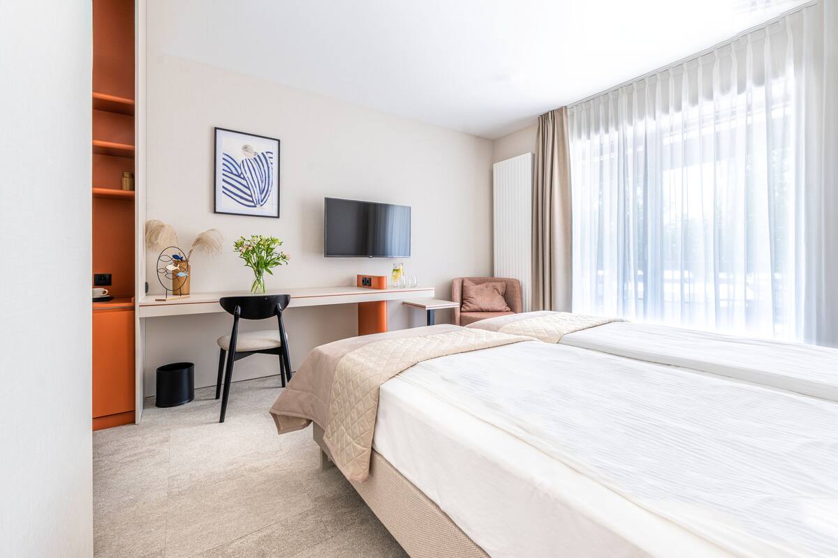 Ein Hotelzimmer mit Bett, Schreibtisch, Stuhl, Fernseher und einem Fenster mit Vorhängen.
